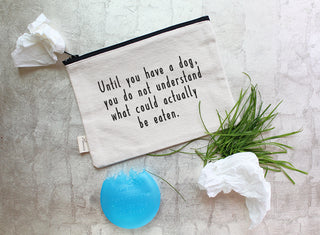 The dog zipper pouch shown styled with grass, kleenex, and a chewed up dog squeaker.