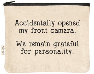 Natural canvas zipper pouch with a black YKK zipper, printed in black with "Accidentally opened my front camera. We remain grateful for personality."