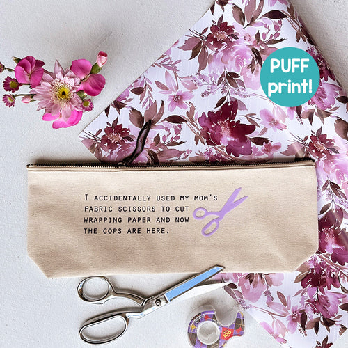 Cotton canvas zip pouch printed with "I accidentally used my mom's fabric scissors to cut wrapping paper and now the cops are here" in black text with lavender puff ink detail.