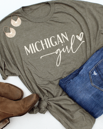 Green t-shirt with 'Michigan Girl' text, blue jeans, and brown boots on a white background