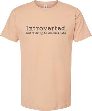 Peach t-shirt with text 'Introverted, but willing to discuss cats' printed in gray ink.