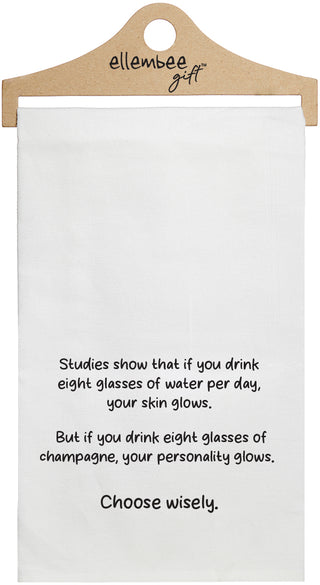 White towel with printed text 'Studies show that if you drink eight glasses of water daily, your skin glows. But if you drink eight glasses of champagne, your personality glows. Choose wisely.' printed in black ink.