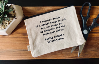 The cut bangs zipper pouch shown styled with scissors and a plant.