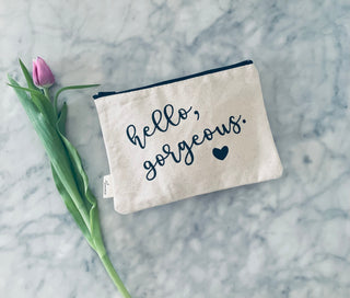 A lifestyle shot of the "hello gorgeous" canvas makeup bag with a tulip next to it.