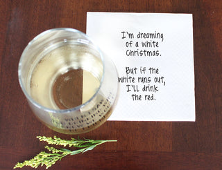 Lifestyle shot of white 3-ply cocktail napkin printed in black with "I'm dreaming of a white Christmas. But if the white runs out, I'll drink the red." glass of white wine.
