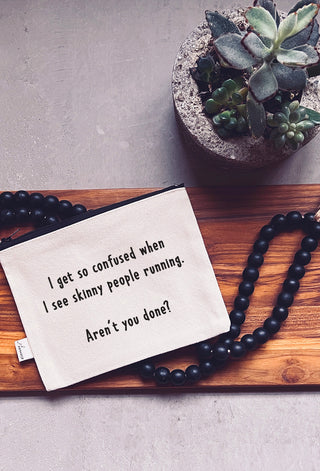 The skinny people running zipper pouch shown styled with a plant, wood, and a string of decorative beads.